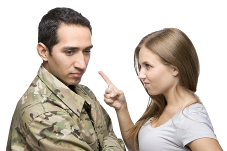 A man in military uniform stands with his arms crossed, looking to the side while a woman shakes her finger at him